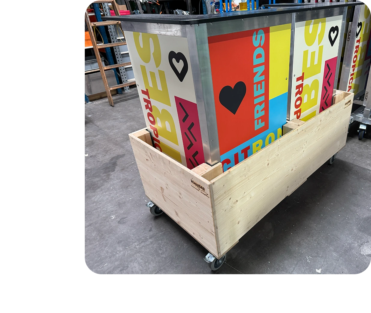 Colorfully branded klappECKE 90° units stacked on a transport cart inside a vibrant festival tent with signage for music, drinks, and chill zones.